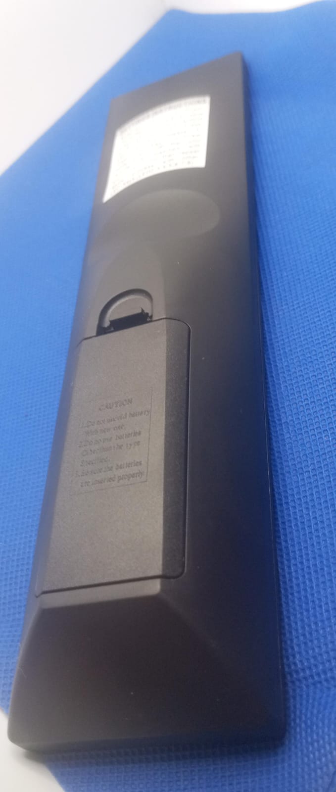 Universal remote control shown from the back, highlighting battery compartment and ergonomic design on a blue background.